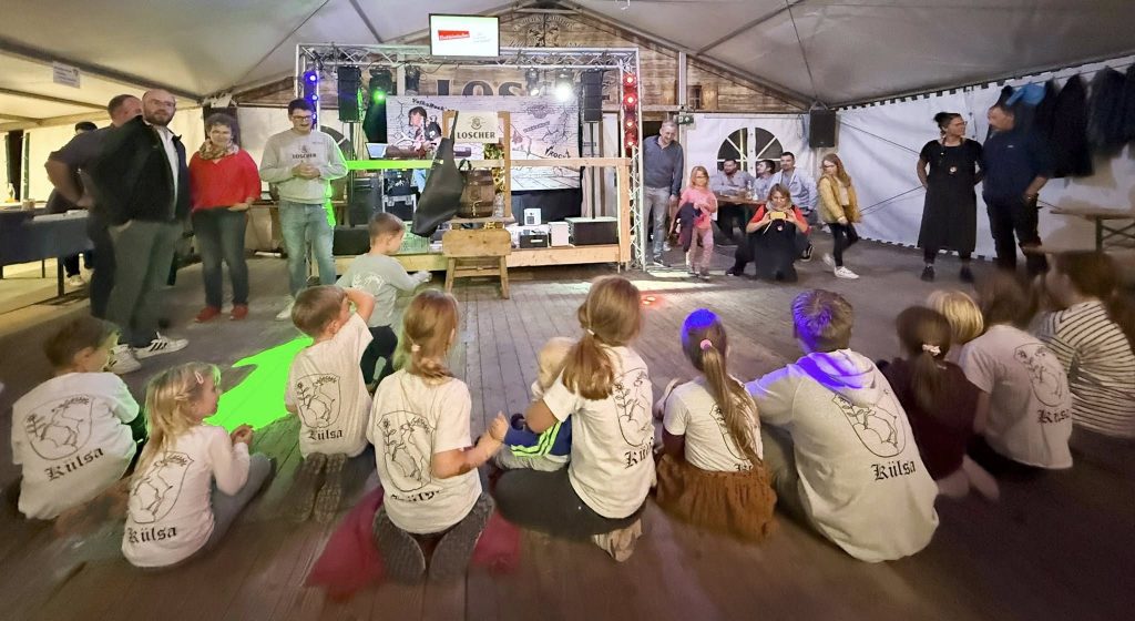 Kinder sitzen im Bierzelt auf dem Boden und hören dem Bürgermeister zu