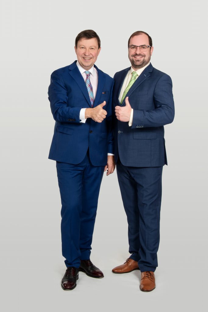 1-25-0220-10-001-005 Jürgen Heckel-Dr. Enz Jürgen Heckel und Dr. Christian Enz in blauen Anzügen vor hellem Hintergrund