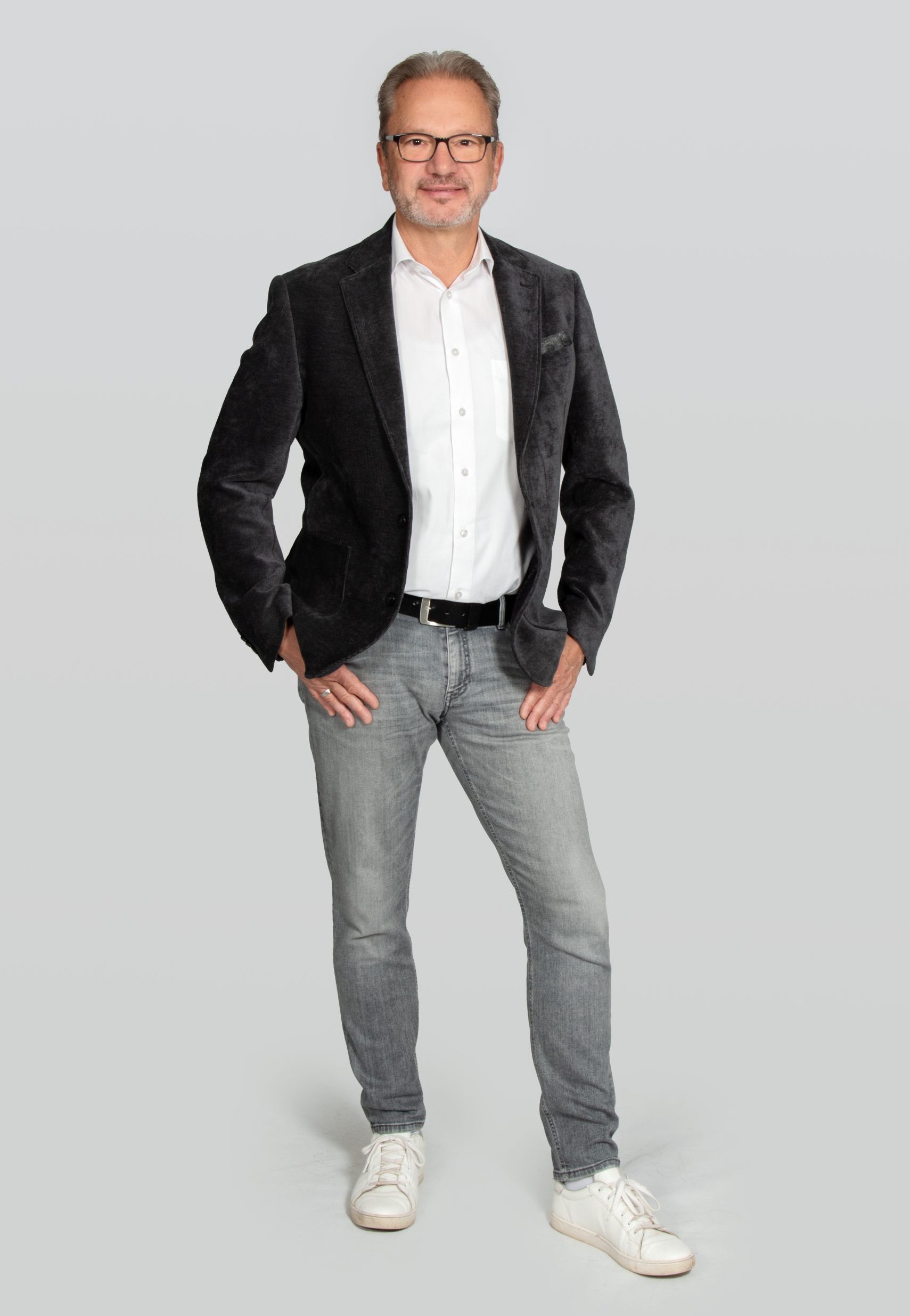 1-25-0220-10-018-003 Frank Mölder Frank Mölcer mit schwarzem Sakko, weißem Hemd und grauer Jeans vor hellem Hintergrund