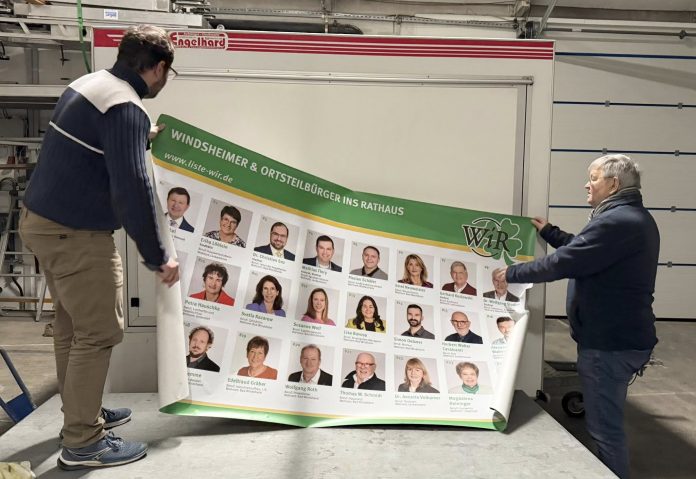 Gerhard Koslowski und Dr. Christian Enz bekleben den Wahl-Anhänger mit Bildern der Kandidaten