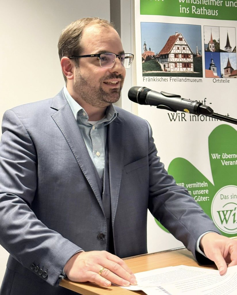 Dr. Christian Enz am Rednerpult vor einem Wahlplakat